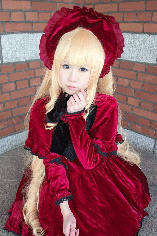 1girl bangs blonde_hair blue_eyes blunt_bangs bonnet brick_wall chain-link_fence closed_mouth dress drill_hair fence frills honeycomb_(pattern) long_hair long_sleeves looking_at_viewer outdoors pavement red_dress shinku sitting solo tile_floor tile_wall tiles wall