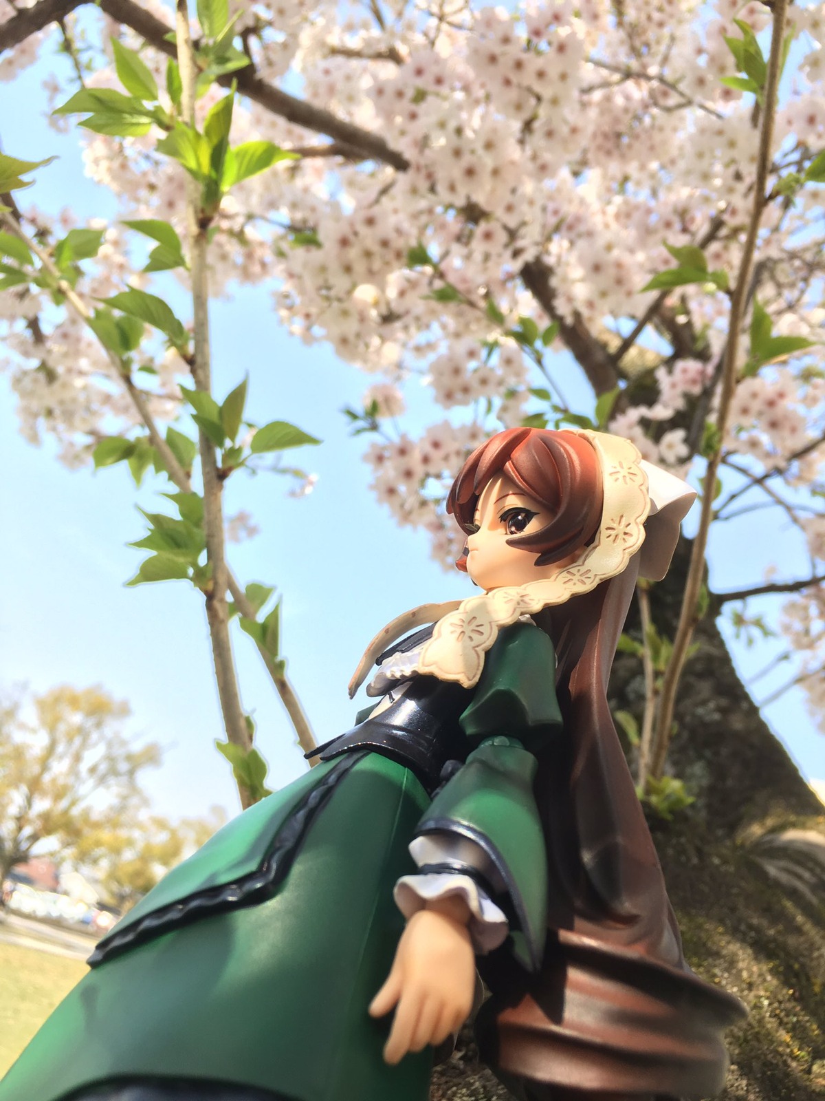 1girl blue_sky blurry blurry_foreground brown_eyes brown_hair cloud day depth_of_field doll dress flower frills green_dress long_hair long_sleeves outdoors puffy_sleeves sky solo suiseiseki tree very_long_hair