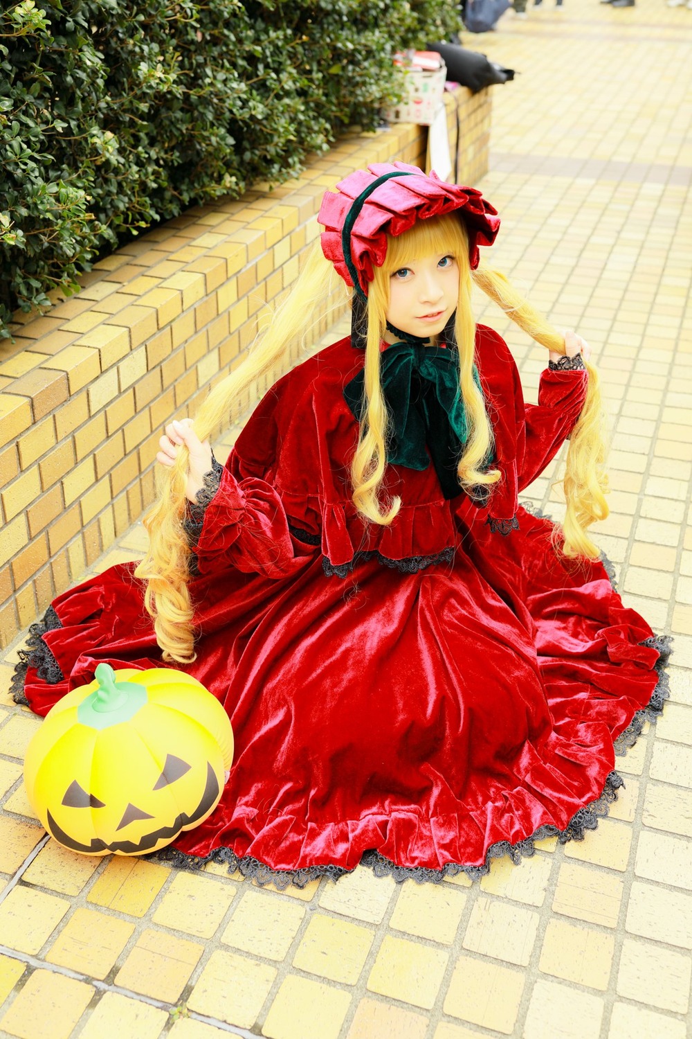 1girl blonde_hair blue_eyes bonnet dress fence frills jack-o'-lantern long_hair long_sleeves looking_at_viewer outdoors pumpkin red_dress shinku sitting solo tile_floor tiles