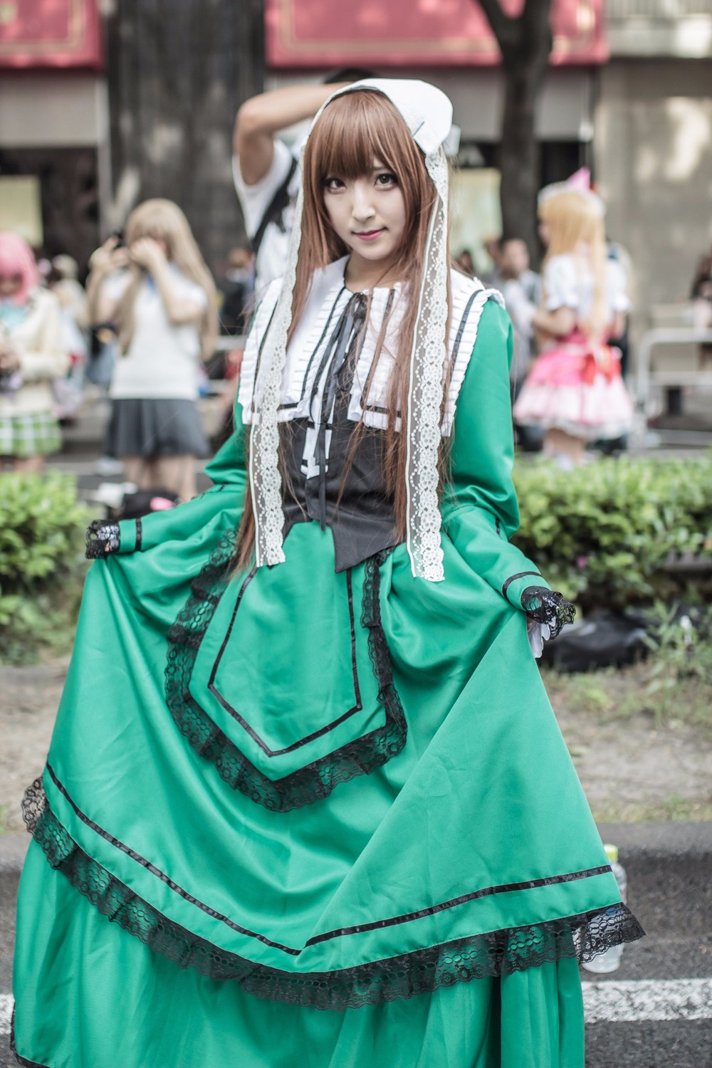 3d blurry blurry_background blurry_foreground brown_hair day depth_of_field dress figure green_dress long_hair multiple_girls outdoors photo photo_background realistic solo solo_focus standing suiseiseki