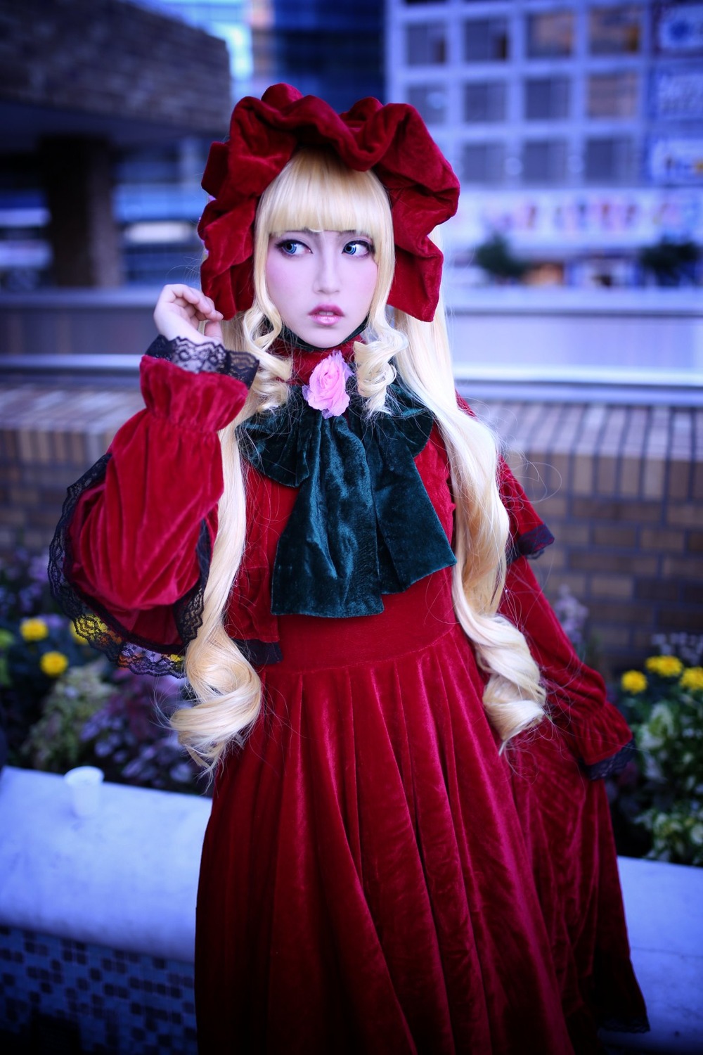 1girl bangs blonde_hair blue_eyes blurry blurry_background bonnet building depth_of_field dress expressionless flower long_hair long_sleeves photo red_dress shinku solo standing