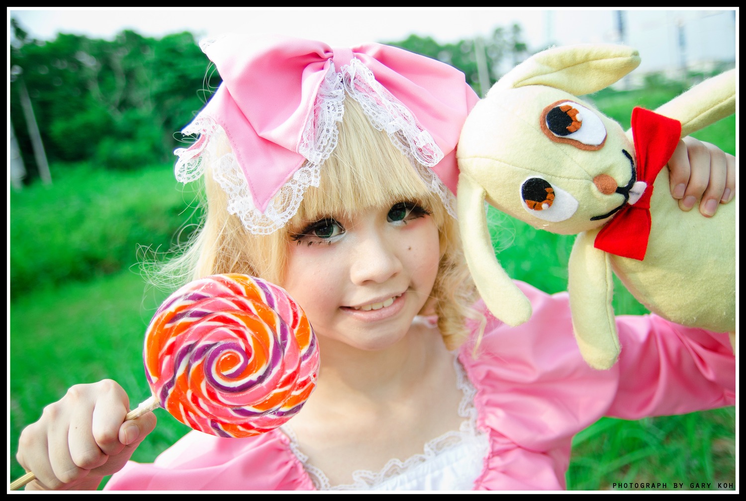 1girl black_border blonde_hair border bow candy day food hinaichigo holding_food letterboxed lollipop outdoors smile solo swirl_lollipop windowboxed