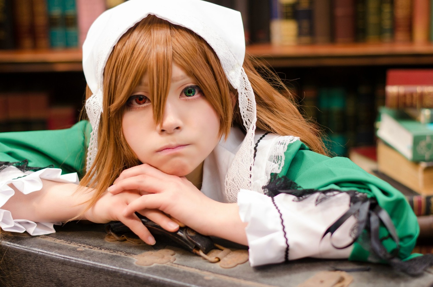 1girl blonde_hair blurry blurry_background bookshelf depth_of_field green_dress green_eyes heterochromia lips long_hair looking_at_viewer solo suiseiseki