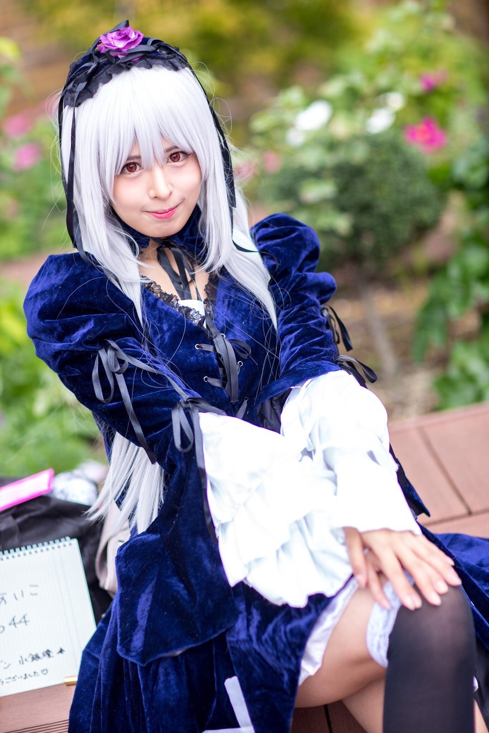 1girl black_legwear blurry blurry_background depth_of_field dress flower frills gothic_lolita hairband lips lolita_fashion long_hair long_sleeves looking_at_viewer photo red_eyes sitting solo suigintou white_hair