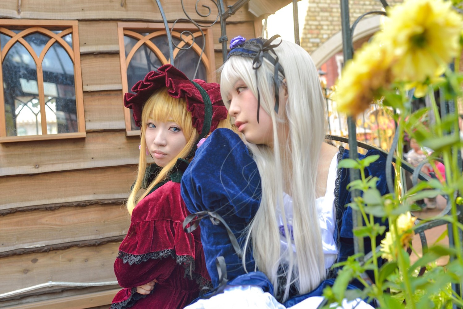 2girls blonde_hair blue_eyes blurry blurry_foreground building depth_of_field dress flower hat lips long_hair long_sleeves looking_at_viewer multiple_cosplay multiple_girls photo red_dress shinku tagme window