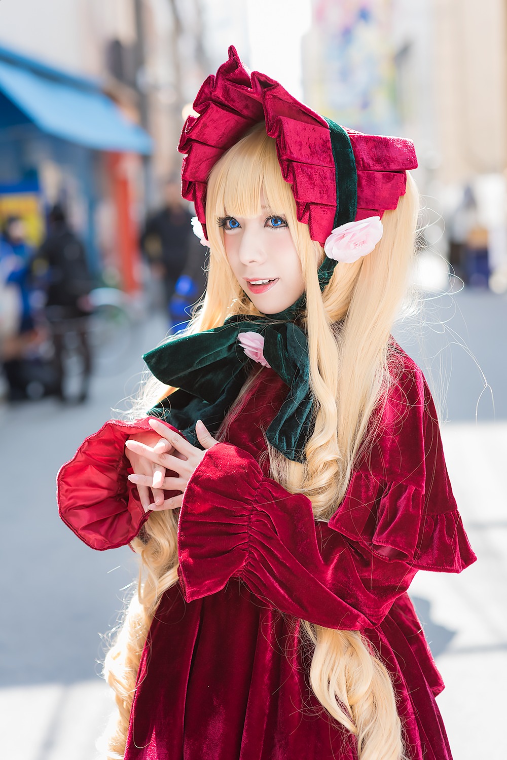 1girl bangs blonde_hair blue_eyes blurry blurry_background blurry_foreground bonnet depth_of_field hands_together long_hair long_sleeves looking_at_viewer outdoors parted_lips shinku smile solo