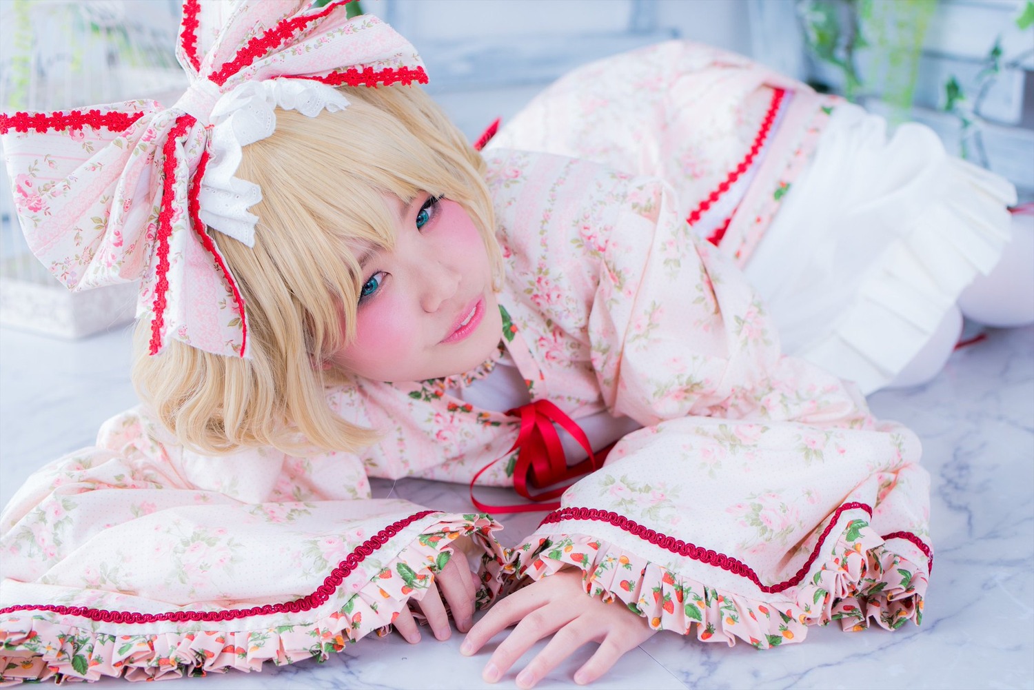 1girl blonde_hair blue_eyes blurry bow day depth_of_field eyelashes flower hair_ribbon hinaichigo lips looking_at_viewer lying medicine_melancholy on_stomach photo ribbon short_hair smile solo