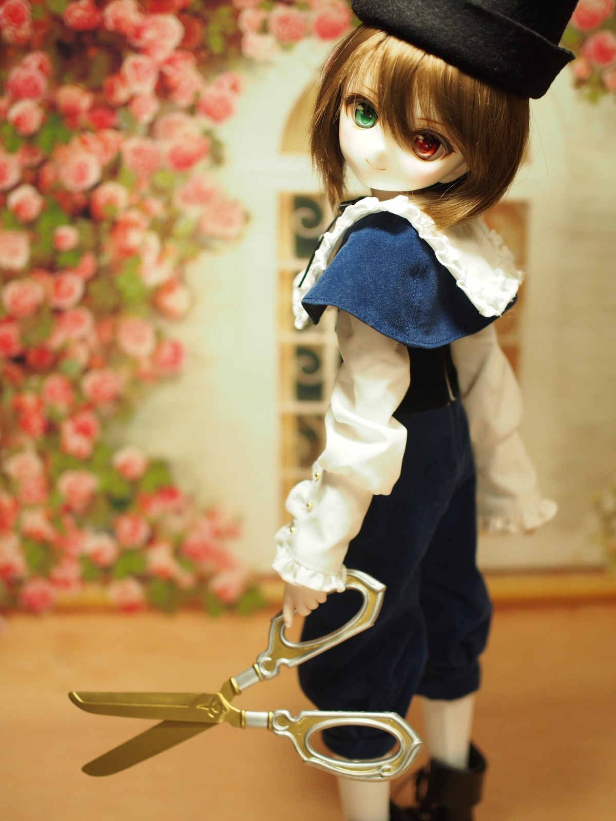 1girl blue_dress blurry blurry_background blurry_foreground brown_hair capelet depth_of_field doll flower fur_trim green_eyes hat heterochromia long_sleeves looking_at_viewer looking_back photo red_eyes red_flower red_rose rose short_hair solo souseiseki standing