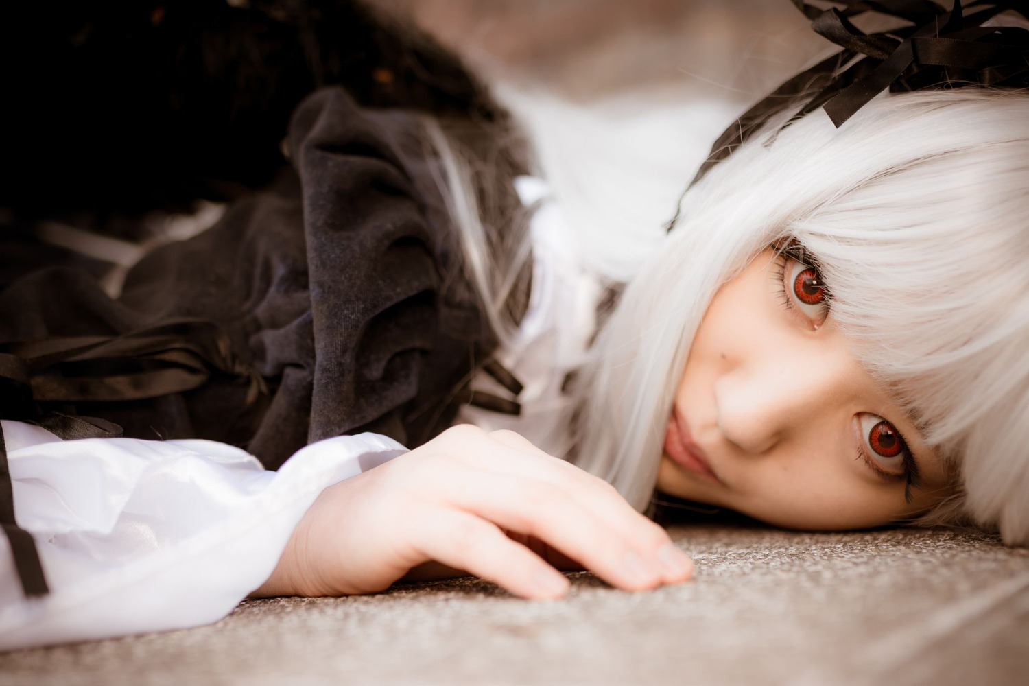1girl bangs blurry closed_mouth depth_of_field lips long_sleeves looking_at_viewer on_stomach red_eyes ribbon smile solo suigintou white_hair