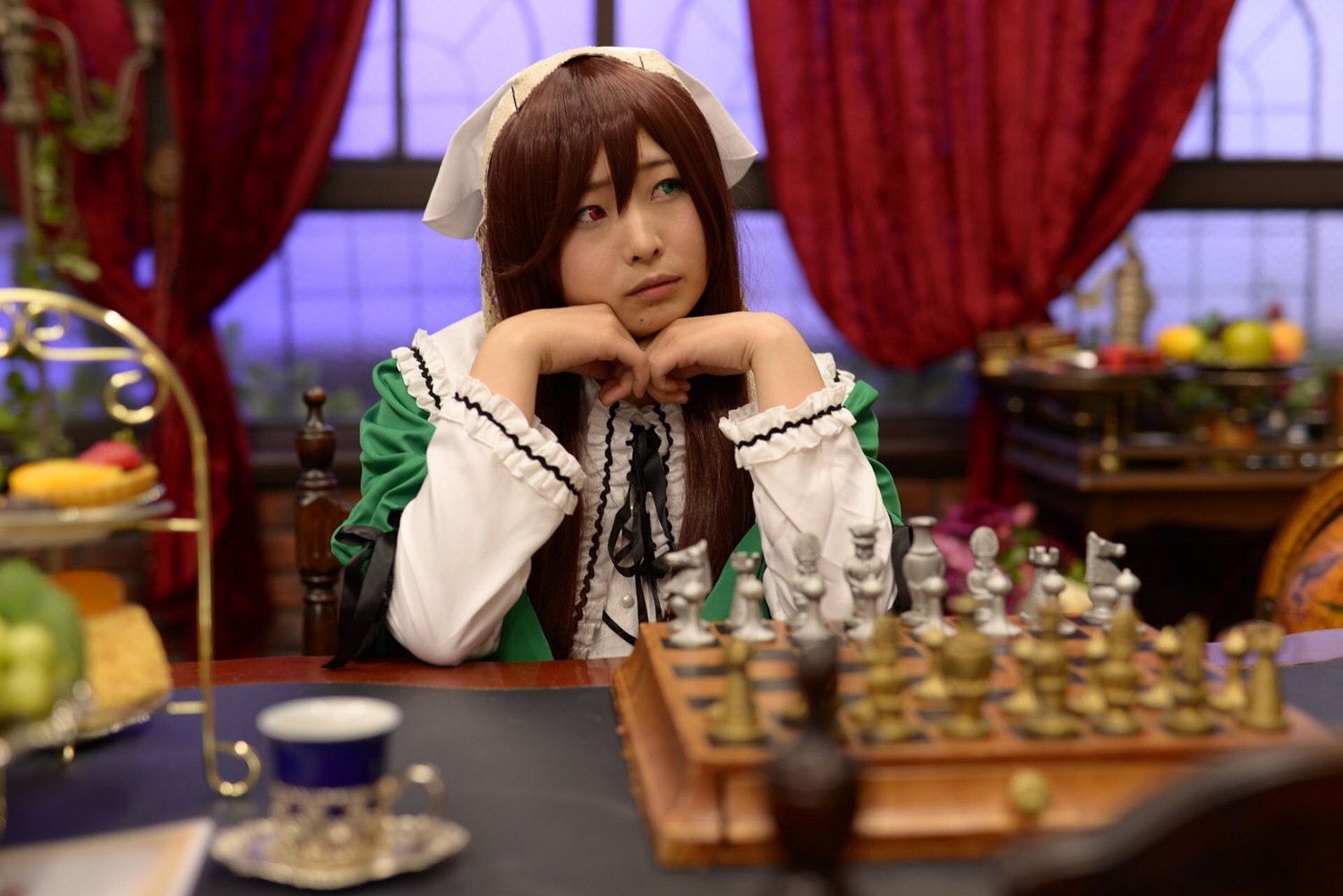 1girl blurry blurry_background blurry_foreground brown_hair curtains depth_of_field dress green_eyes heterochromia indoors long_hair looking_at_viewer red_eyes sitting solo suiseiseki window
