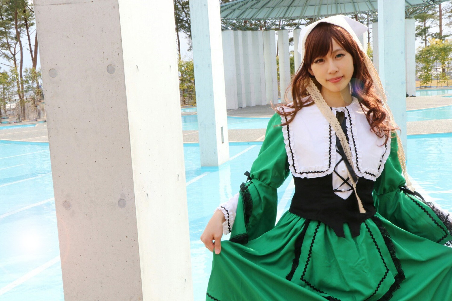 1girl brown_hair building day dress green_dress long_hair long_sleeves looking_at_viewer outdoors skirt_hold smile solo suiseiseki tree