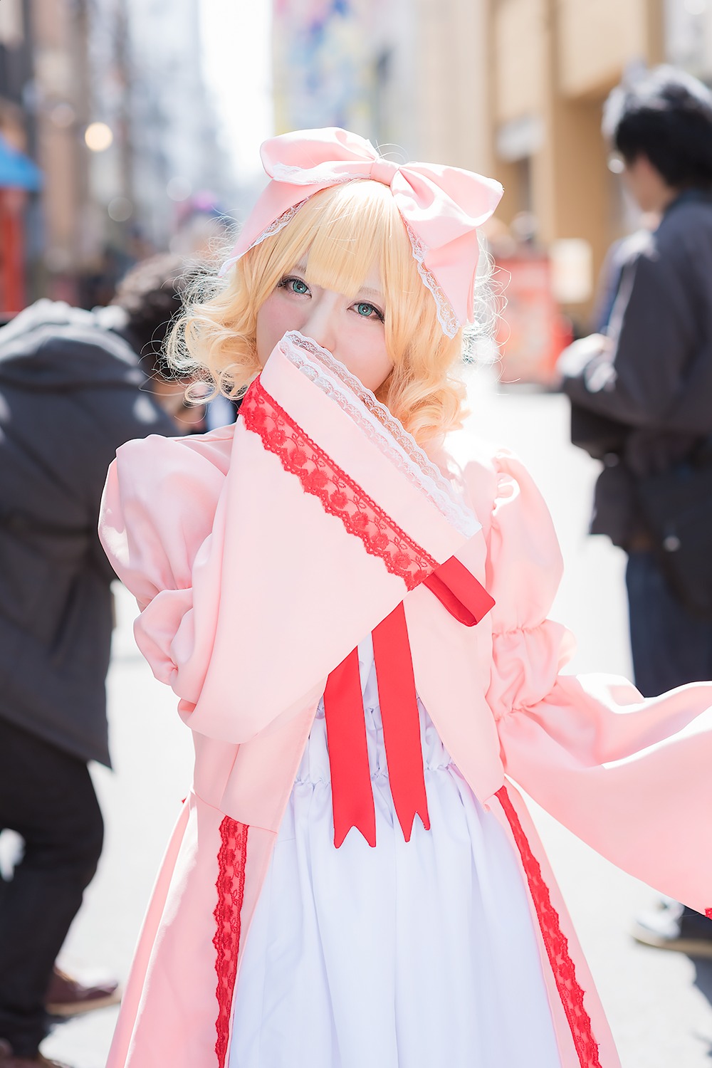 bangs blonde_hair blue_eyes blurry blurry_background blurry_foreground bow capelet clothes_hanger depth_of_field dress frills hair_bow hinaichigo looking_at_viewer motion_blur multiple_girls photo pink_bow pink_dress pink_scarf short_hair solo solo_focus