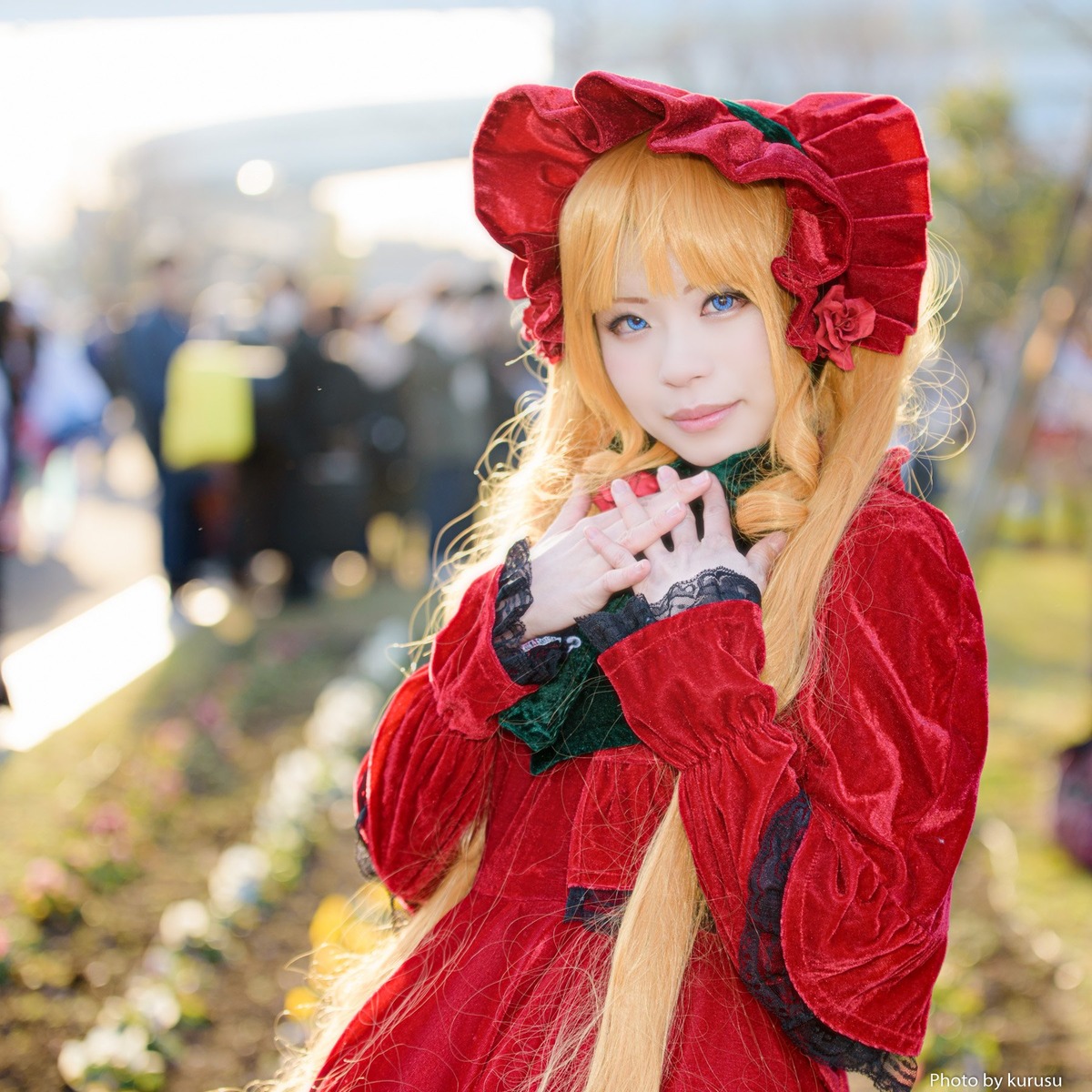 1girl artist_name bangs blonde_hair blue_eyes blurry blurry_background blurry_foreground bonnet depth_of_field dress flower hat long_hair long_sleeves looking_at_viewer outdoors photo red_dress shinku solo watermark
