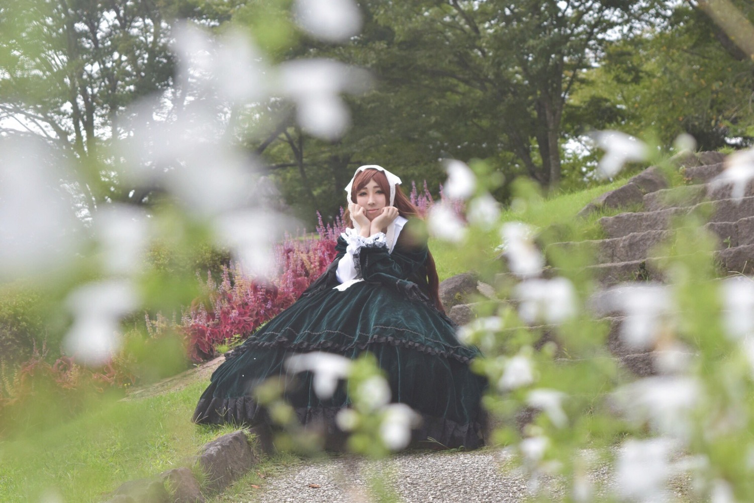 1girl black_dress blurry blurry_foreground brown_hair depth_of_field dress flower grass long_hair long_sleeves outdoors solo suiseiseki