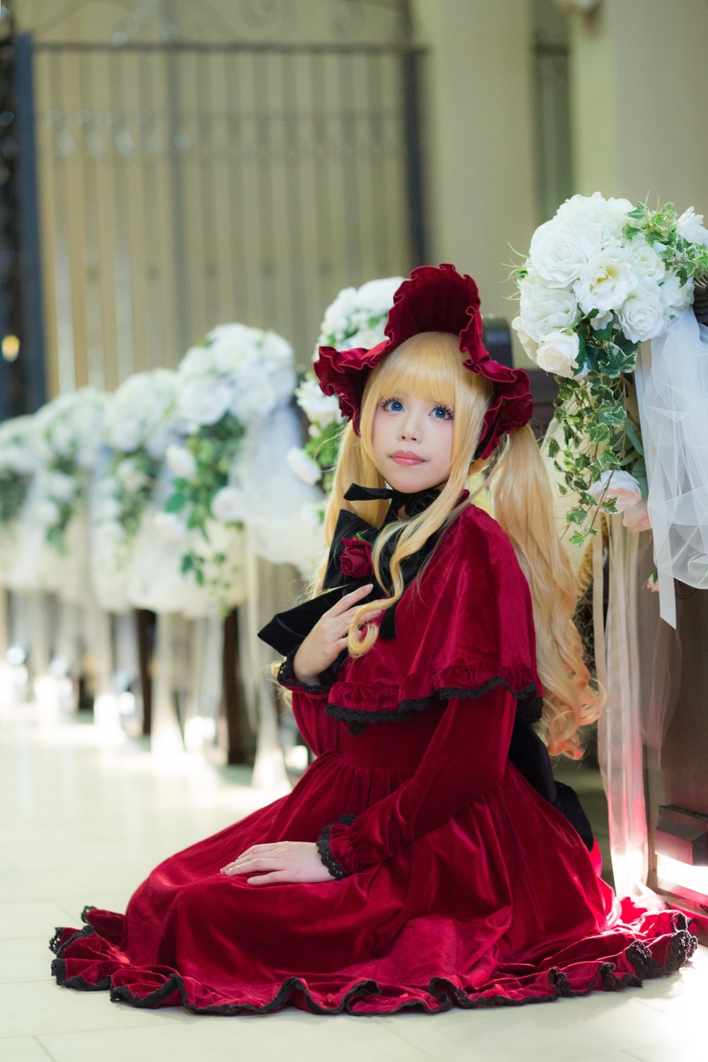 1girl blonde_hair blue_eyes blurry blurry_background bonnet depth_of_field dress flower lips long_hair long_sleeves photo red_dress rose shinku sitting solo