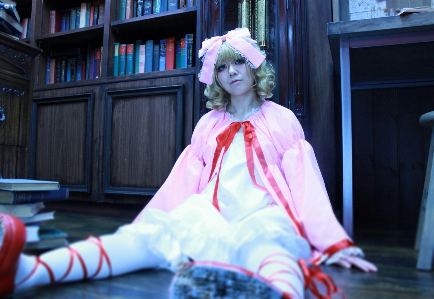 1girl blonde_hair blue_eyes blurry blurry_foreground book book_stack bookshelf depth_of_field dress hinaichigo indoors library lips photo ribbon sitting solo