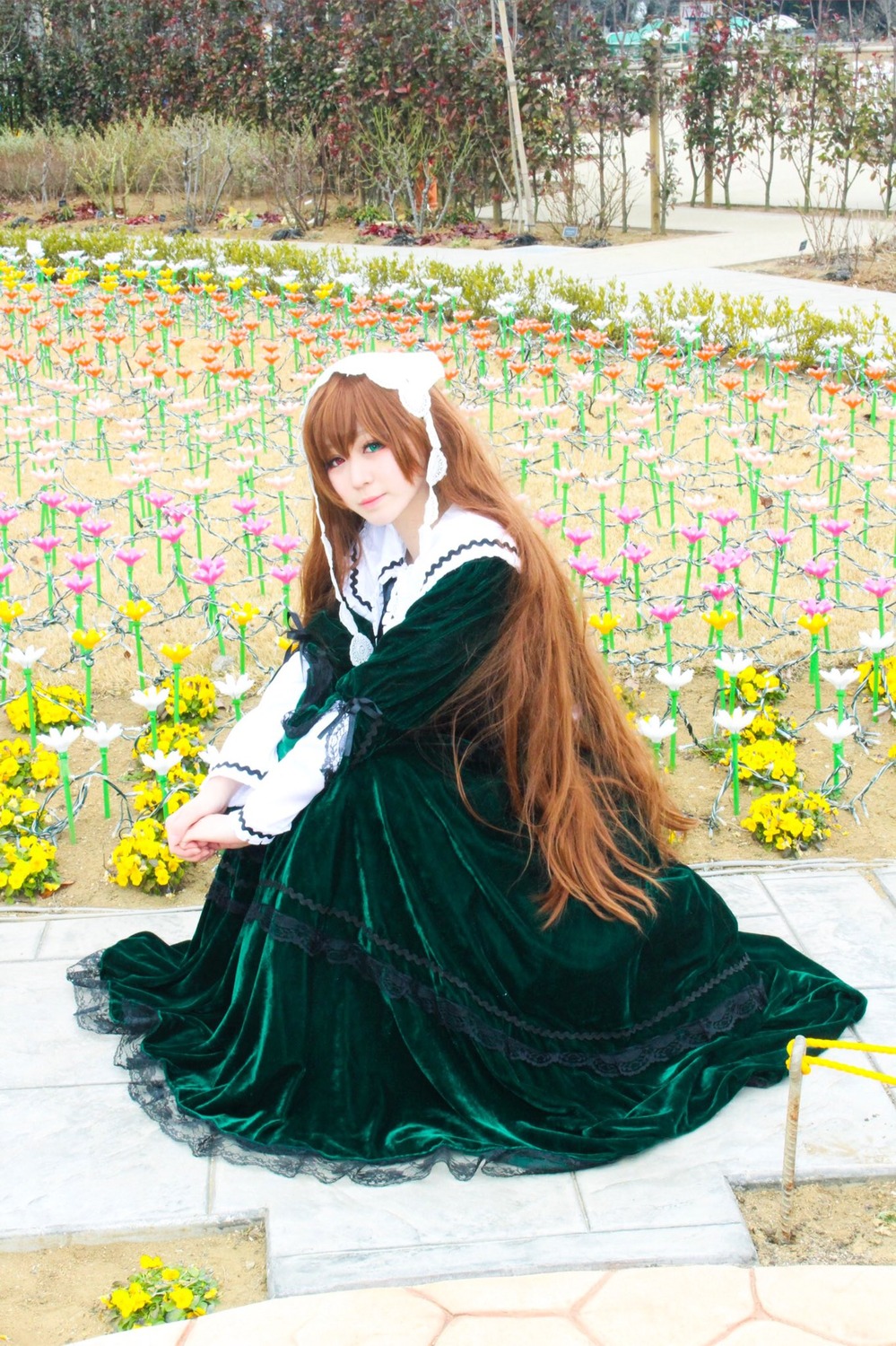 1girl blonde_hair brown_hair dress flower garden green_dress green_eyes long_hair long_sleeves looking_at_viewer solo suiseiseki tile_floor tiles very_long_hair yellow_flower
